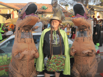 Dinoman Steve wearing his green cape with kids in T-rex costumes on either side of him.