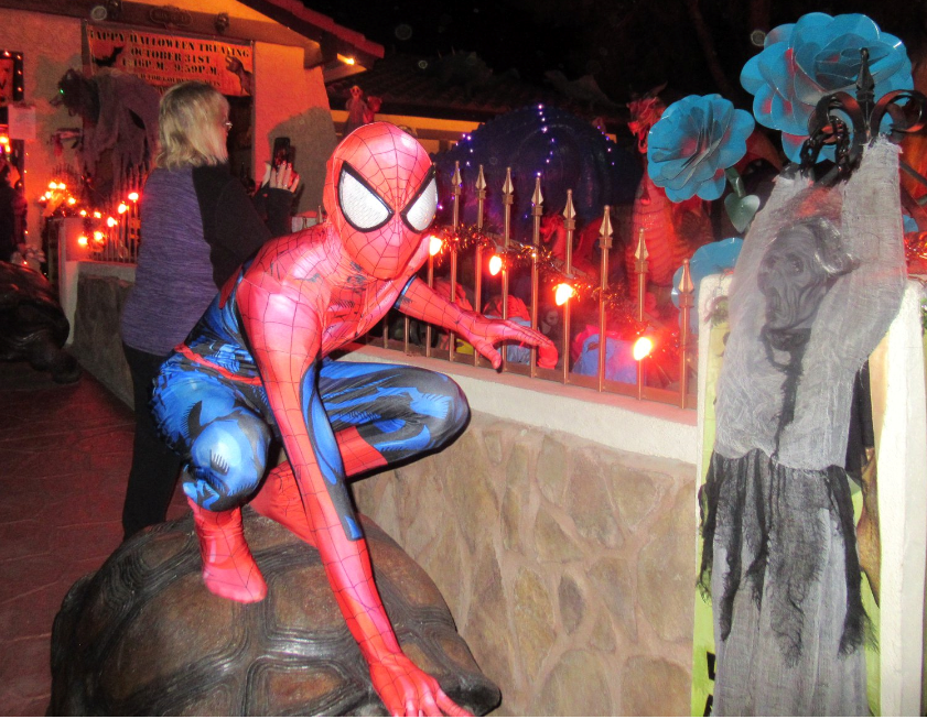 A young person dressed in a spiderman costume of red and blue, crouched on top of a giant tortoise statue ready to jump into action. 